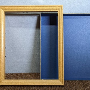 May include: A wooden picture frame with a blue cardboard backing. The frame is empty and ready for a picture.