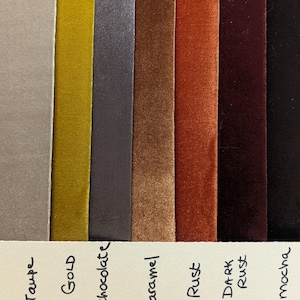 May include: Seven vertical strips of velvet ribbon in shades of taupe, gold, chocolate, caramel, rust, dark rust, and mocha. Below each ribbon, the corresponding color name is handwritten in black ink on a light cream-colored paper strip.