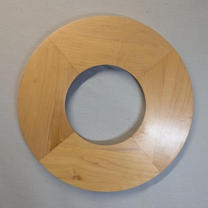 May include: A circular wooden frame with a central hole. The frame is constructed from light-colored wood, with visible grain patterns. The design features a geometric pattern, with the circle divided into segments.