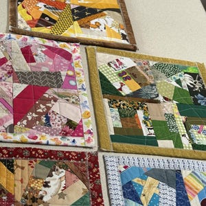 May include: Five square fabric quilts featuring a crazy quilt patchwork design with various patterned cotton fabrics in yellow, pink, green, red, and blue colour schemes, each finished with a coordinating fabric border and visible machine quilting.