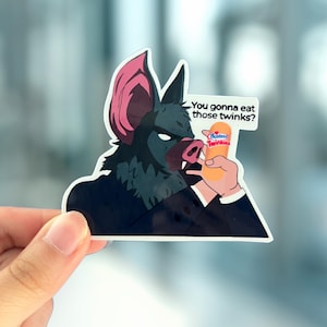 May include: A sticker featuring a bat-like creature in a suit holding a Hostess Twinkie. The bat has pink ears and a pig-like snout. Text on the sticker reads, "You gonna eat those twinks?"