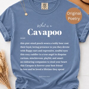 May include: A blue short-sleeved t-shirt featuring white text that defines a Cavapoo as a pint-sized pooch with a teddy bear coat, floppy ears, and soulful eyes. The graphic includes the words What is a Cavapoo, noun, and a poem about the dog.