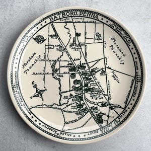 May include: A cream-colored decorative plate featuring a detailed map of Hatboro, Pennsylvania, with street names and landmarks in dark green. The plate includes text around the border, such as "Hatboro Borough Incorporated 1871".