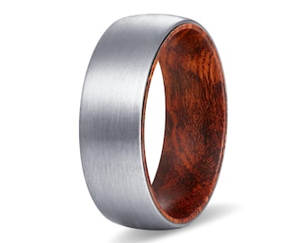 May include: A ring featuring a brushed silver-toned metal exterior with a smooth, matte finish and a contrasting inner band made of dark reddish-brown wood with a visible, natural grain pattern throughout the interior surface of the ring.