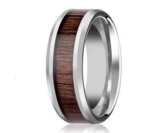 May include: A polished silver-toned metal ring featuring a wide, flat band with bevelled edges and a central inlay of dark brown wood grain. The metallic surface is reflective, contrasting with the textured, organic appearance of the wood.