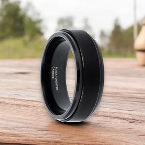 May include: A black tungsten carbide ring with a beveled edge and a brushed finish. The ring is engraved with "BLACK TUNGSTEN CARBIDE".