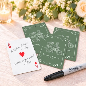 Op de afbeelding: Een witte speelkaart met de rode tekst A lifetime of love! - Lily, Cheers to you both! - Alex, en rode harten, naast drie saliegroene kaarten met witte lijntekeningen van een koppel op een fiets en de tekst William & Julia 16.05.26.
