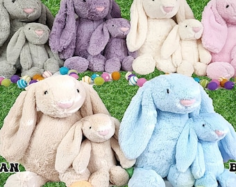 May include: A collection of plush bunny rabbits in various colors: gray, purple, ivory, pink, tan, and blue. Each bunny has long floppy ears and a soft, cuddly appearance. Easter eggs are scattered around the bunnies on a green background.