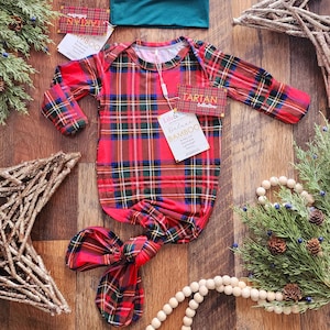 May include: Red and green plaid baby knotted gown and matching hat. The gown has long sleeves and a knotted bottom. The hat has a green brim. The text on the tag reads "Deluxe Bamboo Tartan Collection".