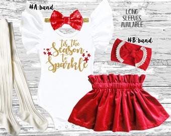 May include: A festive baby outfit set featuring a white bodysuit with gold glitter text reading "Tis the Season to Sparkle", a red velvet skirt, and a red sequin bow headband. Includes white tights and a second red headband.