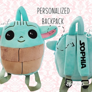 May include: A turquoise plush backpack with a cartoon character on the front and the name "SOPHIA" embroidered on the back. The backpack has a green strap and a pink ear.