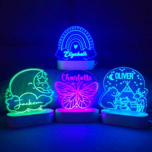 May include: Three colorful night lights with personalized names. The first light is a rainbow with the name "Elizabeth" on it. The second light is a butterfly with the name "Charlotte" on it. The third light is a moon and clouds with the name "Jackson" on it.