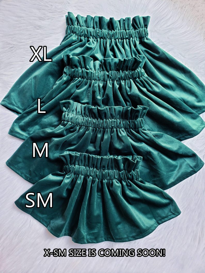 Four dark green velvet skirts stacked vertically on a white surface, labeled with sizes XL, L, M, and SM, with text at the bottom stating that X-SM size is coming soon.