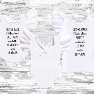 Three white children's garments displayed on a wood background, showcasing cross-back flutter-sleeve leotards and shirts with overlaid text describing available sizes.