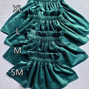 May include: Four green velvet skirts in different sizes: XL, L, M, and SM. The skirt is gathered at the waist and has a ruffled hem. The text "X-SM size is coming soon!" is printed at the bottom of the image.