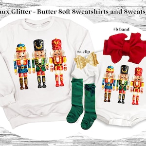 May include: A white sweatshirt and bodysuit with a glittery nutcracker design. The sweatshirt has three nutcrackers, while the bodysuit has three nutcrackers. The bodysuit also has a red bow headband.