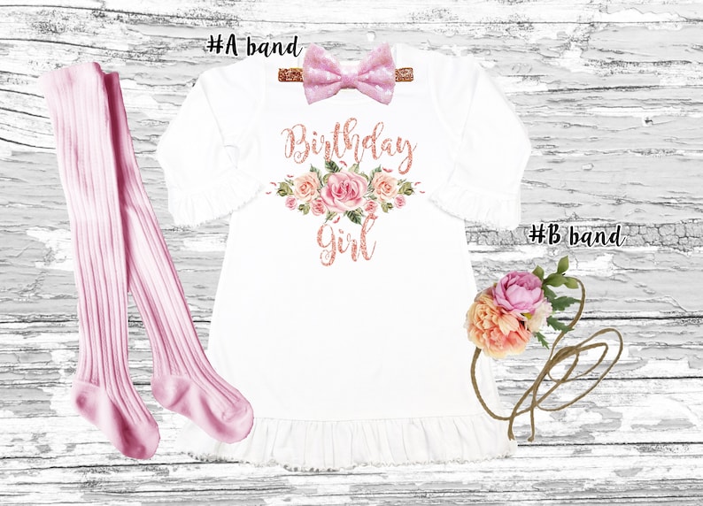 K&ouml;nnte beinhalten: Ein wei&szlig;es Kleid mit einem rosafarbenen Blumendesign und dem Text "Birthday Girl" in ros&eacute;goldenen Glitzer. Das Kleid hat einen R&uuml;schen-Saum und wird mit einem rosafarbenen Schleifen-Haarreif und rosafarbenen Strumpfhosen geliefert.