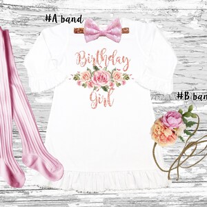 K&ouml;nnte beinhalten: Ein wei&szlig;es Kleid mit einem rosafarbenen Blumendesign und dem Text "Birthday Girl" in ros&eacute;goldenen Glitzer. Das Kleid hat einen R&uuml;schen-Saum und wird mit einem rosafarbenen Schleifen-Haarreif und rosafarbenen Strumpfhosen geliefert.