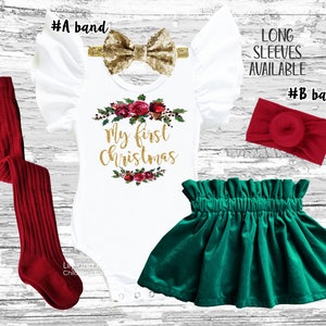 May include: A white bodysuit with the text "My First Christmas" in gold glitter, surrounded by a wreath of red roses and green leaves. The bodysuit has ruffled sleeves and is paired with a green velvet skirt and red tights. Two headbands are included, one gold glitter bow and one red.