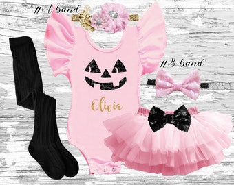 May include: Pink baby outfit with a black and gold pumpkin face, the name Olivia, and a black bow. The outfit includes a tutu, a headband, and leggings.
