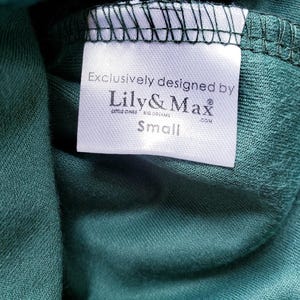 A clothing tag sewn inside a green fabric garment, featuring the text Exclusively designed by Lily and Max with the size Small below it.