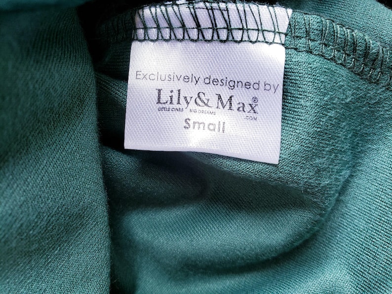 A clothing tag sewn inside a green fabric garment, featuring the text Exclusively designed by Lily and Max with the size Small below it.