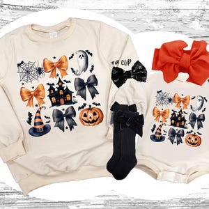 May include: A set of two cream-colored Halloween shirts with a variety of spooky and festive designs, including pumpkins, ghosts, witches hats, and houses. The larger shirt has the text "#a clip" and the smaller shirt has the text "#b band".