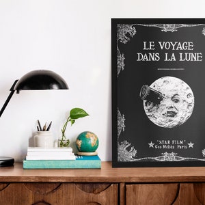 Puede incluir: Un p&oacute;ster en blanco y negro con un dise&ntilde;o vintage que presenta una luna con una cara mirando a trav&eacute;s de un telescopio. El texto en el p&oacute;ster dice "Le Voyage Dans La Lune" y "Star Film Geo M&egrave;li&egrave;s Paris".