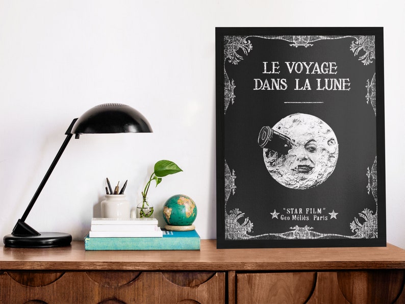 Puede incluir: Un p&oacute;ster en blanco y negro con un dise&ntilde;o vintage que presenta una luna con una cara mirando a trav&eacute;s de un telescopio. El texto en el p&oacute;ster dice "Le Voyage Dans La Lune" y "Star Film Geo M&egrave;li&egrave;s Paris".