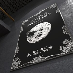 Puede incluir: Un p&oacute;ster en blanco y negro con el t&iacute;tulo "Le Voyage Dans La Lune" y un dibujo de la cara de un hombre en la luna. El texto "Star Film" y "Geo Melies Paris" tambi&eacute;n est&aacute; en el p&oacute;ster.