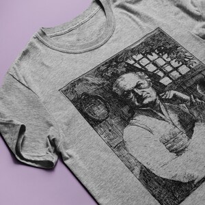 May include: A gray t-shirt with a black and white illustration of a man with a beard. The illustration is in a square frame and shows the man looking to the side.