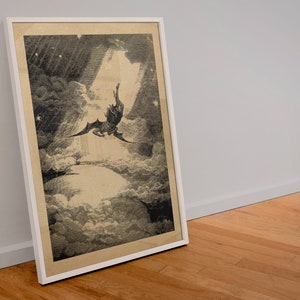 Puede incluir: Obra de arte en blanco y negro enmarcada que representa una figura alada cayendo a trav&eacute;s de las nubes, con un rayo de luz que brilla hacia abajo. La obra de arte est&aacute; en un marco blanco y se apoya contra una pared blanca y un suelo de madera.