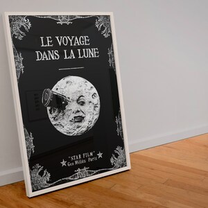 Puede incluir: Un p&oacute;ster en blanco y negro con un marco blanco. El p&oacute;ster presenta un fondo negro con texto blanco que dice "LE VOYAGE DANS LA LUNE" y una imagen blanca de la luna con una cara y un telescopio. El texto en la parte inferior dice "STAR FILM - Geo. Melies Paris."