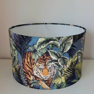 May include: A lampshade featuring a blue background with a tiger print. The tiger is surrounded by green and yellow tropical leaves.