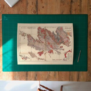 May include: A vintage map of the British Isles, printed on paper, is laid out on a green cutting mat. The map is surrounded by a wooden table surface.