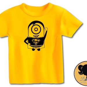 K&ouml;nnte beinhalten: Ein gelbes T-Shirt mit einer schwarzen Silhouette eines Minions, der einen Superman-Umhang und ein Logo tr&auml;gt. Der Minion l&auml;chelt und hat einen Arm erhoben.