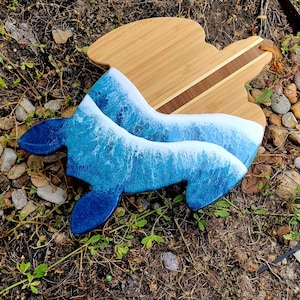 May include: A wooden cutting board with a blue and white resin ocean wave design. The board has a natural wood finish and a brown wood inlay.