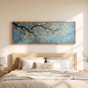 May include: A rectangular wall art piece featuring a dark tree branch with golden leaves against a textured blue background, enclosed in a light wood frame. The text ART NOVA GALERIA is visible on a small rectangular pillow on the bed below.