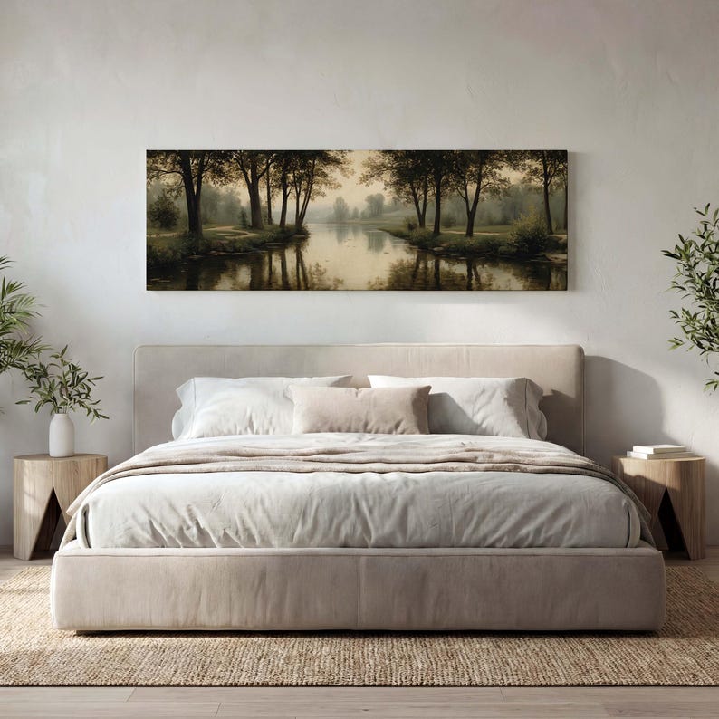 Puede incluir: Un cuadro panor&aacute;mico de paisaje que muestra un r&iacute;o tranquilo que fluye a trav&eacute;s de un bosque con &aacute;rboles de color verde oscuro y sus reflejos en el agua, colocado sobre una cama tapizada en beige con ropa de cama blanca y dos mesitas de noche.