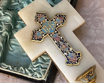 May include: A white marble cross with a gold-trimmed, enameled cross laid on top. The enameled cross features blue, purple, and gold floral designs and the letters IHS. A small, matching gold and enamel piece is also present.