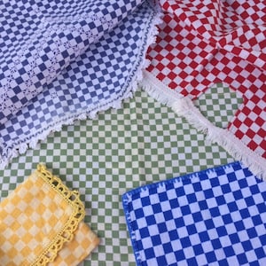 May include: A collection of checkered fabric pieces featuring a blue and white cloth with a lace edge, a red and white cloth with a fringed edge, a yellow and white cloth with a crocheted border, and a green and white checkered base fabric.