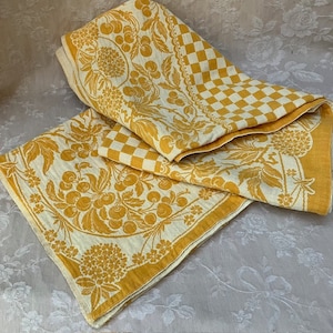 Può includere: Strofinacci da cucina vintage gialli e crema. Uno presenta un motivo a scacchiera, l'altro un design floreale e di ciliegie. Gli strofinacci sono piegati e disposti su una superficie bianca.