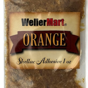 May include: A small, clear plastic bag filled with orange shellac flakes. The bag has a label that reads "WellerMart" in red letters and "ORANGE Shellac Adhesive 1 oz" in brown lettering.