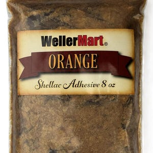 May include: A clear plastic bag filled with orange shellac adhesive. The bag has a label with the words "WellerMart ORANGE Shellac Adhesive 8 oz" in a vintage style. The shellac adhesive is a light brown color.