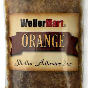 May include: A clear plastic bag filled with orange shellac flakes. The bag has a label that reads "WellerMart" in red letters and "ORANGE" in large yellow letters. The label also says "Shellac Adhesive 2 oz".