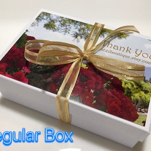 May include: White gift box with a gold ribbon and a floral design on the lid. The lid has the text "Thank You" and a website address. The box is tied with a gold ribbon.
