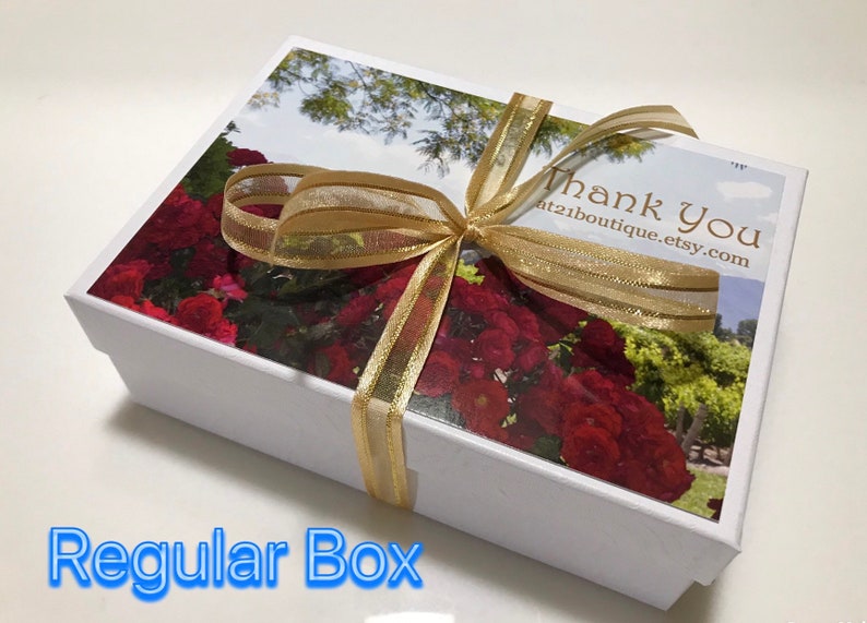 May include: White gift box with a gold ribbon and a floral design on the lid. The lid has the text "Thank You" and a website address. The box is tied with a gold ribbon.