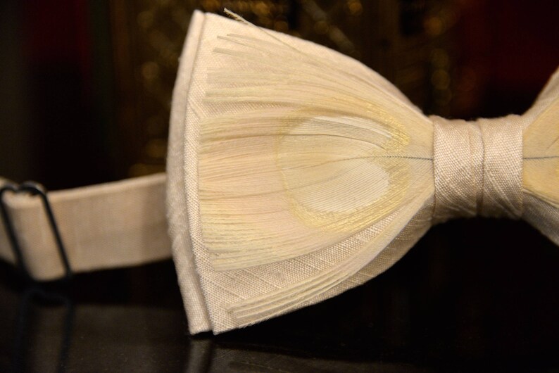 May include: A white bow tie made of feathers with a satin band. The bow tie is tied and ready to wear.