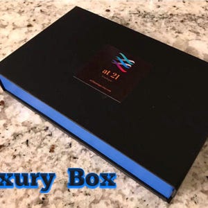 May include: A black box with a blue trim. The box has a logo on the top that says "at 21" with a colorful design. The box is on a white and gray countertop.