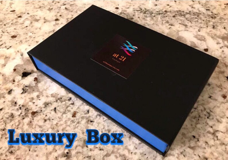 May include: A black box with a blue trim. The box has a logo on the top that says "at 21" with a colorful design. The box is on a white and gray countertop.